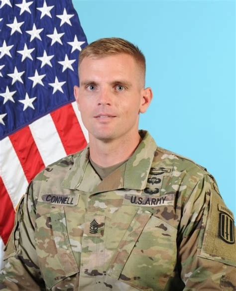 A soldier in uniform, standing in front of a flag