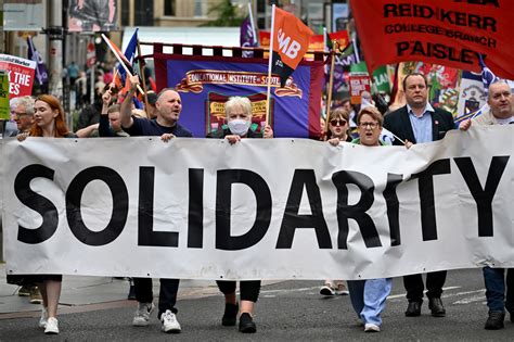 Workers on strike holding signs that read 'Fair Pay Now'